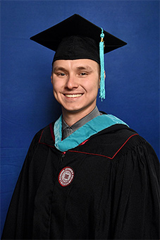 Alexander Clausius in graduation cap and gown in front of blue background