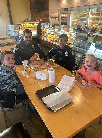 Ingrid Ortega and a fellow officer in uniform having donuts with two kids at a donut shop
