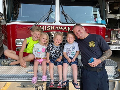Josh Jester and his children in front of a Mishawaka Fire Department fire engine with another fire engine in the background