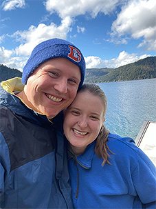 Zachary McClure and his wife smiling with blue sky, clouds, and mountains in the background